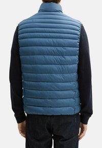 Blauwe gewatteerde vest met een staande kraag en horizontale quiltstructuur. De stof lijkt lichtgewicht en glad, met een ritssluiting aan de voorkant.