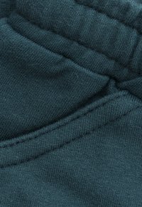 Close-up van donkerblauw groen gebreide stof met dichte stiksels, naden en details van een verzameld elastische tailleband.