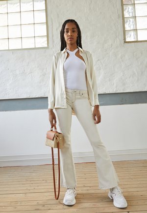 Camisa de seda branca, top branco canelado, jeans cream de boca de sino, sapatilhas brancas com detalhes, bolsa de vime com trim em pele castanha.
