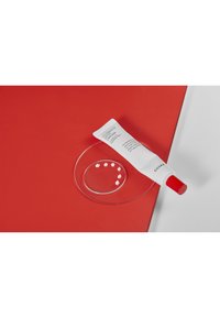 Tube cosmétique blanc étiqué "Crème Hydratante Ultime" avec un capuchon rouge, placé sur une assiette en verre ronde sur fond rouge.
