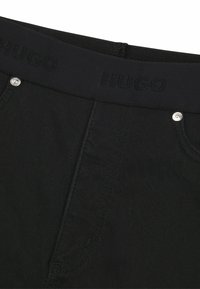 Jeans in denim nero con una cintura spessa caratterizzata dal logo "HUGO", ferri resistenti e una superficie liscia e opaca.