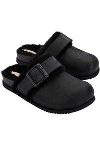 Black clogs made of textured material with a fuzzy interior, featuring a side strap with a buckle and a flat rubber sole.