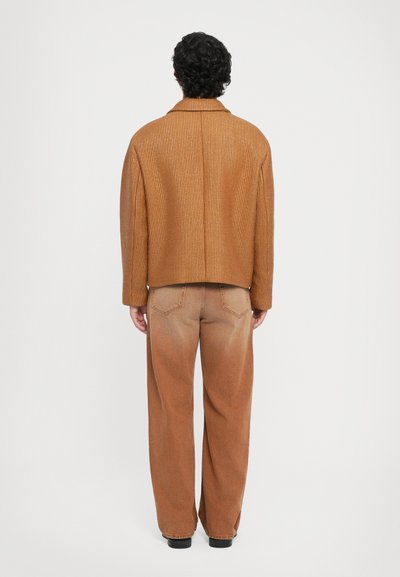 Chaqueta marrón de canalé con corte recto y mangas anchas, combinada con pantalones anchos marrones desgastados. No se observan patrones prominentes ni elementos metálicos.