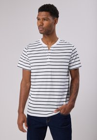 Valkoinen lyhythihainen t-paita, jossa on mustia vaakaraitoja, varustettuna nappikiinnitteisellä henley-kauluksella ja rennolla istuvuudella.