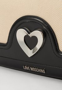Black and beige handbag with a patterned canvas body, featuring a silver heart-shaped hardware accent and embossed branding.