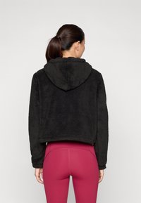 Hoodie in pile nera cropped con cappuccio, tessuto texturizzato e maniche lunghe, abbinato a leggings rosa a vita alta.