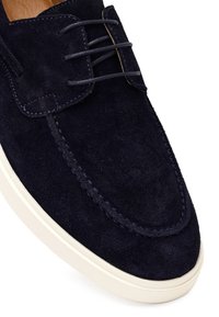 Granatowy zamszowy but na sznurówki z przeszyciami w stylu mokasynów i białą gumową podeszwą, widoczny z bliska od przodu i z boku.