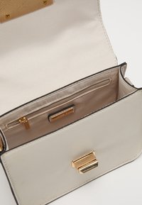 Borsa a mano in pelle color crema con finitura testurizzata, hardware dorato e interno rivestito in satin con tasca con zip.