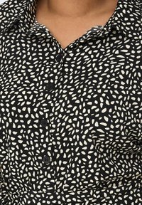 Chemise noire avec un col, ornée d'un motif de points abstraits blancs, de cinq boutons noirs et d'un tissu texturé.