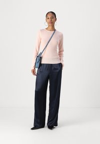 Maglione rosa chiaro a coste, pantaloni ampi in satin blu navy e una piccola borsa a tracolla blu. Il modello indossa scarpe nere a punta e orecchini a cerchio.