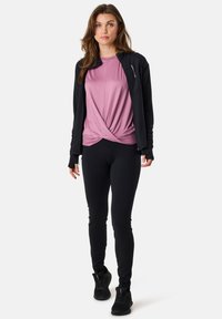 Black athletic jacket, pink short-sleeve shirt with knot design, black leggings, and black sneakers. Smooth texture, fitted design.