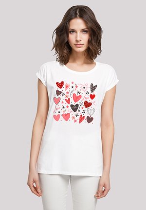 White cotton t-shirt featuring a colorful heart and star print in shades of red, black, and pink. Short sleeves and a round neckline.