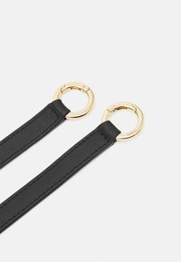 Correa de cuero negro con dos anillas circulares en tono dorado en los extremos, que muestra una textura suave y detalles de costura limpios.