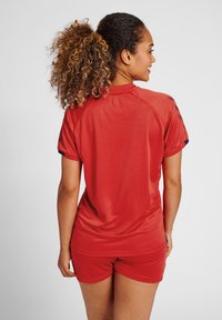 Rotes Sportoutfit bestehend aus einem Kurzarmshirt und Shorts, gefertigt aus glattem Stoff mit lockerer Passform. Enthält marineblaue Akzente an den Ärmeln.