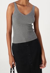 Šedé žebrované tílko s výstřihem do V a širokými ramínky. Nošeno s černou sukní s vysokým pasem, zdůrazňující texturu a střih.