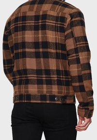 Veste en flanelle à carreaux bruns et noirs avec fermeture à boutons, présentant une coupe classique et un tissu texturé, vue de dos.