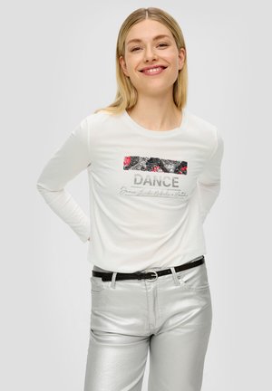 Witte longsleeve shirt met een grafische "DANCE" print in metallic grijs en een bloemenpatroon. Gecombineerd met glanzende zilveren broek en een zwarte riem.