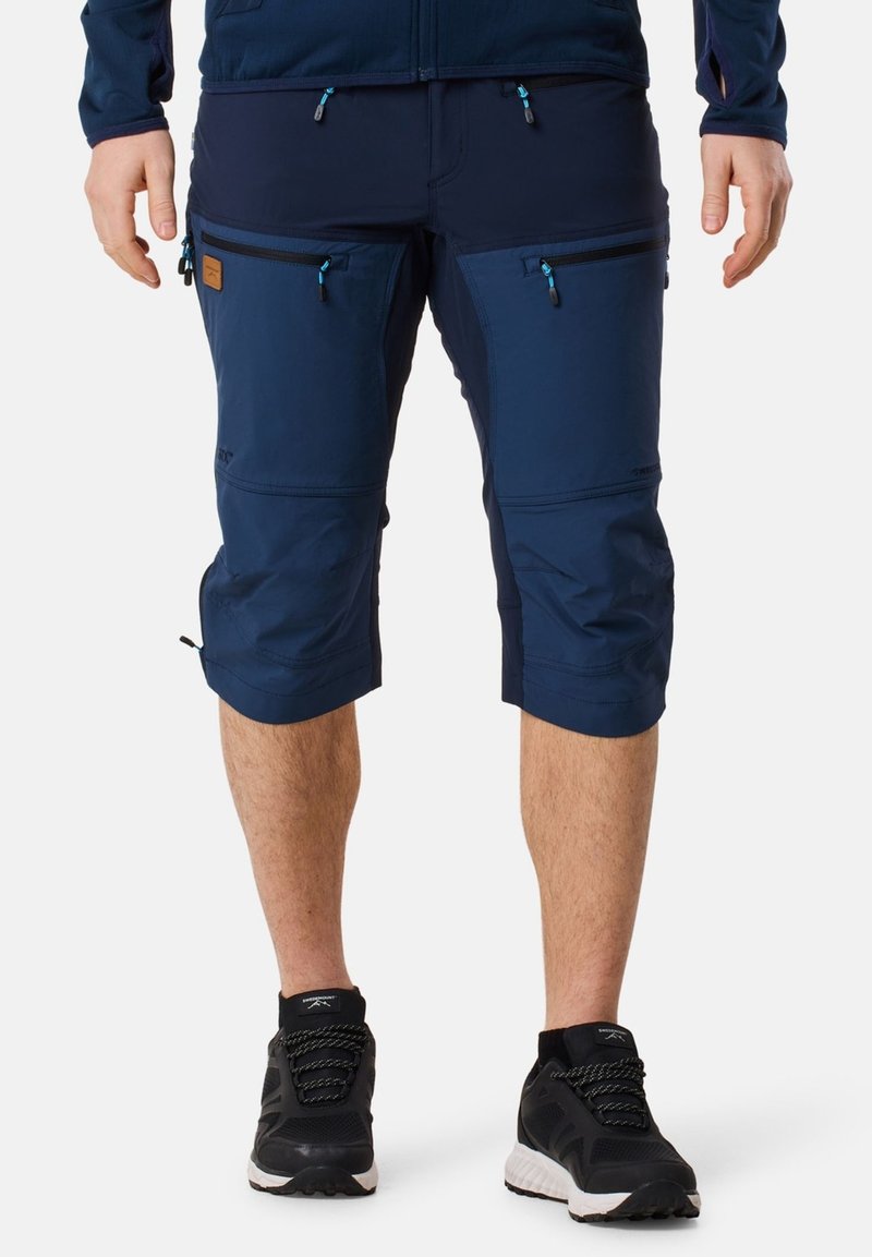 Marinblå knälånga shorts i lätt material, med flera fickor med dragkedja och kontrasterande detaljer vid sömmarna.