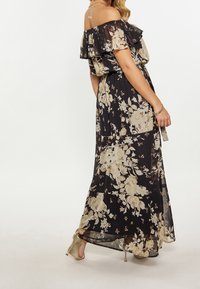 Černé květinové maxi šaty s volánovými rukávy off-shoulder, zdobené světlým květinovým vzorem v krémové a béžové barvě, s lehkým splývavým střihem.