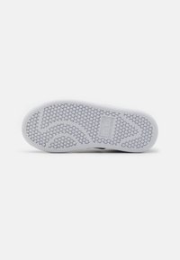 White rubber shoe sole with a textured honeycomb pattern and branded logo. Rounded shape with flex grooves for grip and flexibility.