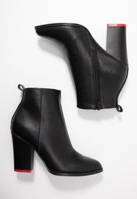 Schwarze Knöchelstiefel aus strukturiertem Leder mit einem Reißverschluss, schmaler Zehenpartie und einem klobigen Absatz, der an der Basis accentuiert ist in Rot.