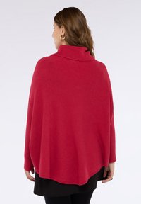 Poncho rosso a maglia con colletto alto, caratterizzato da dettagli a coste sulle maniche. Texture morbida e vestibilità ampia, che scende oltre la linea della vita.