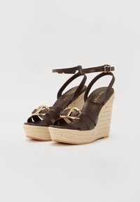 Brown leather wedge sandals with a woven jute platform, featuring a front strap with a gold-tone buckle and ankle strap.