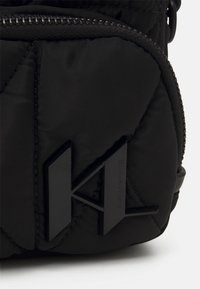 Sort, kviltet nylon taske med et særpræg ved den matte, sorte logo. Lynlåslukning med kontrastsyet og en glat overflade.