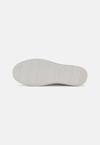 Semelle de sneaker blanche avec des stries horizontales et une texture subtile. Présente le logo "Calvin Klein" près du talon. Design épuré et minimaliste.