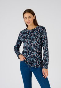Camicia a maniche lunghe blu navale con un motivo floreale in turchese, rosa e bianco. Tessuto morbido, collo rotondo e vestibilità rilassata. Indossata con jeans blu.