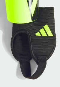 Black fabric shin guard with a bright neon green plastic exterior. Features a textured finish and adjustable strap for secure fit.