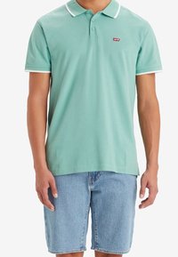 Polo shirt vert menthe avec col et accents de manches blancs, arborant un petit logo rouge Levi's. Associé à un short en denim bleu clair.