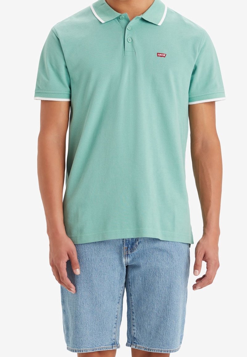 Polo shirt vert menthe avec col et accents de manches blancs, arborant un petit logo rouge Levi's. Associé à un short en denim bleu clair.