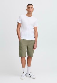 Camiseta blanca de manga corta combinada con pantalones cortos de cargo verde oliva. El modelo lleva calcetines blancos y zapatillas blancas con rayas negras. Diseño y corte sencillo.