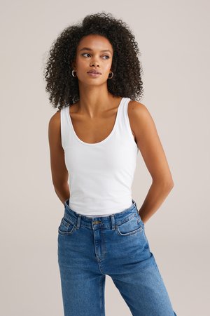 Valge sobiv tank top, millel on laiakujuline kaelus, kombineeritud helesiniste kõrge vöökohtadega denim teksadega. Sile kangas, ilma varrukateta disain, igapäevane stiil.