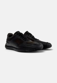 Black athletic shoes with a textured upper, mesh panels, and a thick rubber sole. Features a rounded toe and lace-up design.