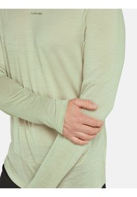 Hellgrünes Langarmshirt aus strukturiertem Stoff, mit Daumenlöchern und entspannter Passform. Dezentes Logo in der Nähe des Ausschnitts.