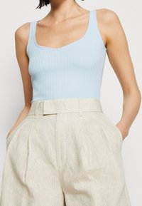 Débardeur bleu clair à côtes avec un col en V, associé à un pantalon beige taille haute à jambes larges avec poches latérales.