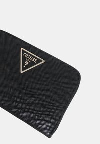 Cartera negra texturizada con un logo triangular plateado "GUESS USA" en el frente y una forma suave y elegante para un manejo fácil.