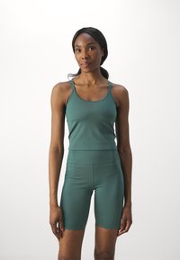 Grønn atletisk tanktop og høyt liv shorts laget av stretchy, glatt stoff, med tynne stropper og en tettsittende design.