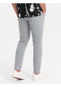Šedé slim-fit joggers vyrobené z texturované látky, s bočními kapsami a zúženým střihem nohavic. Spárovány s bílými teniskami.