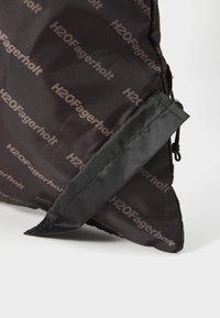 Fekete nylon táska, amelyen az "H2OFagerholt" logó ismétlődő mintázatban található. Fekete szövetpánttal rendelkezik, amely húzózáras záródással ellátott.