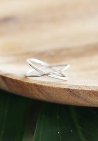 Zilveren ring met een gedraaide, overlappende ontwerp, met een gladde, gepolijste textuur, rustend op een houten oppervlak.