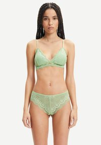 Grünes Spitzen-Unterwäsche-Set mit einem gewellten Bralette und verstellbaren Trägern sowie passendem Slip, das komplizierte Muster und Texturen zeigt.