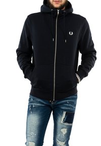 Felpa zipata blu navy con tasche frontali, cappuccio con cordino, polsini a costine e dettaglio del logo sul petto; abbinata a jeans in denim strappati.