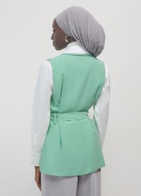 Minzgrüner Blazer mit Taillengürtel, getragen über einem weißen Hemd. Die Rückseite weist eine glatte Textur und eine strukturierte Silhouette auf.