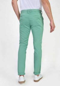 Mintgroene chino's met een slim fit, voorzien van achterzakken en opgerolde zakken, gecombineerd met witte sneakers voor een casual uitstraling.