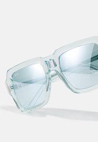 Ochelari de soare transparenti, de culoare albastră, cu lentile mari și unghiulare și un cadru masiv. Au branding subtil și un finisaj neted, lucios.