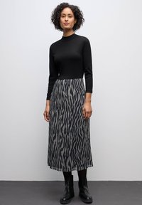 Langes Kleid mit einem engen schwarzen Oberteil und einem fließenden rocklangen Rock, der ein schwarz-weißes Zebramuster aufweist. Strukturierter Stoff.