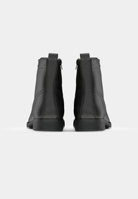 Botas de tobillo de cuero negro con textura suave, costuras mínimas y cremalleras laterales. Suelas de goma con un ligero tacón para mayor tracción.